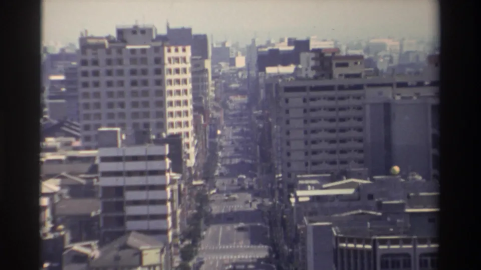 1982 Taiwan urban view from above, with a long avenue, concrete building facades, scattered vehicles, and hazy daylight.