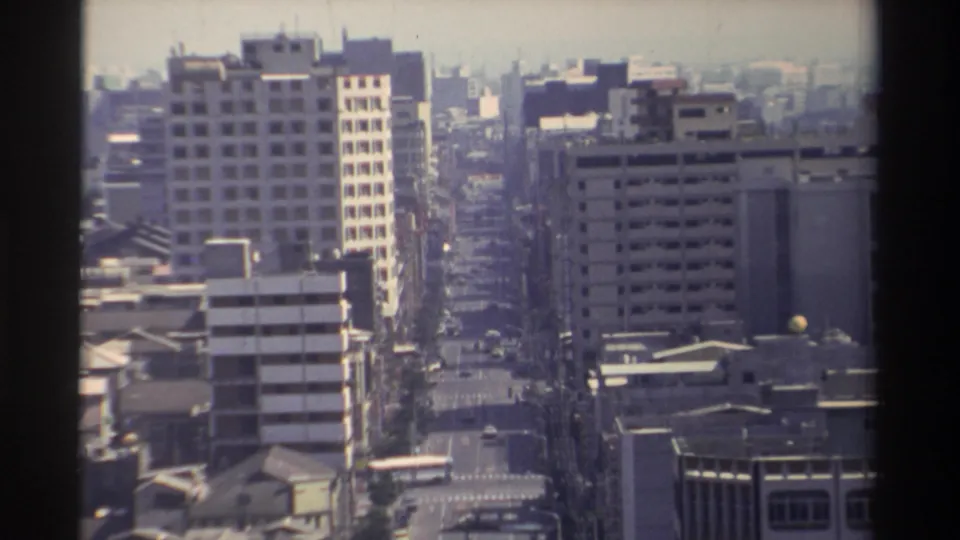 1982 Taiwan city frame with an elevated view of a main road, mid-rise buildings, a bus, and hazy urban distance.