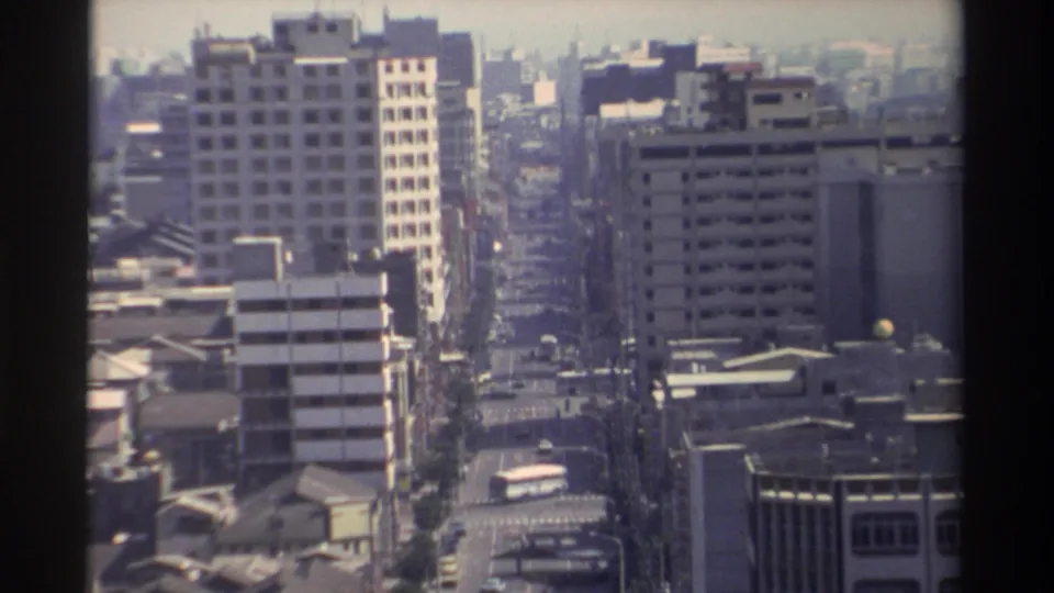 1982 Taiwan home-movie view over a city avenue, showing traffic, grid-like building facades, rooftops, and distant haze.