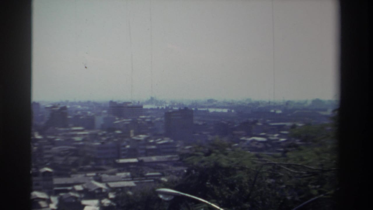1982 Taiwan frame with the camera panning across a distant city, tree canopy in front, and visible small-gauge film borders.