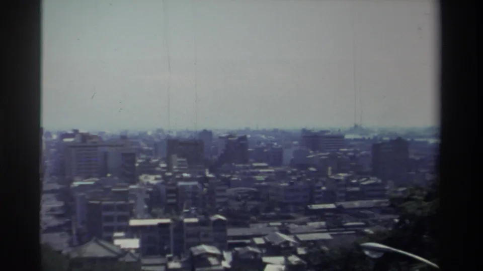 1982 Taiwan frame showing city blocks from an elevated wooded viewpoint, with cool faded color and visible 8mm texture.