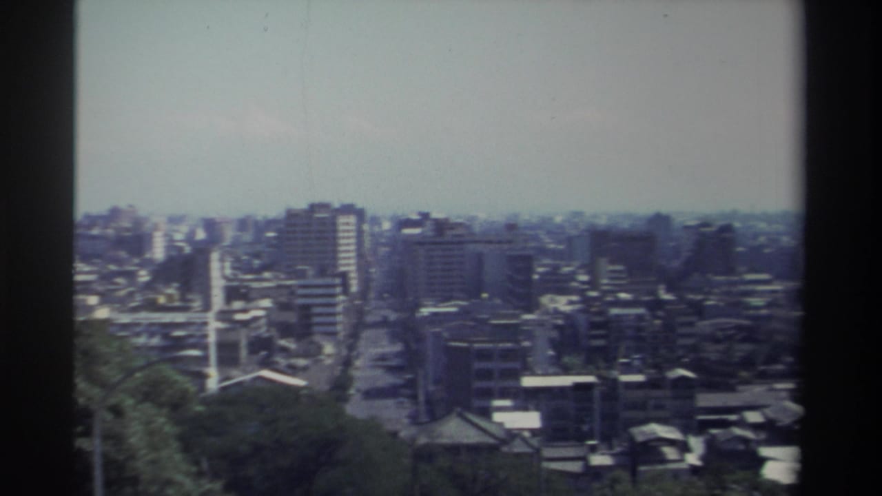 1982 Taiwan frame from an elevated vantage point, looking across dense urban blocks, taller towers, straight streets, and soft blue-green film color.