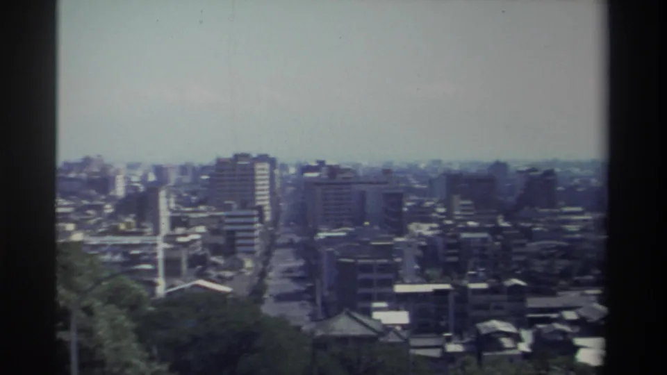 1982 Taiwan frame from an elevated vantage point, looking across dense urban blocks, taller towers, straight streets, and soft blue-green film color.