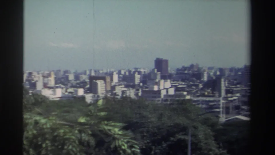 Final 1982 Taiwan frame showing a wider elevated cityscape with foreground greenery, dense white and gray buildings, a dark tower, and soft 8mm color.