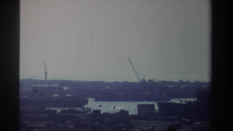 1982 Taiwan home-movie frame showing a distant port landscape with cranes, water, low buildings, and visible aging marks in the film.