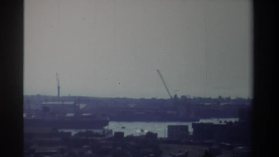 Hazy 1982 Taiwan waterfront frame with cranes and dockside forms visible across the water in soft 8mm focus.