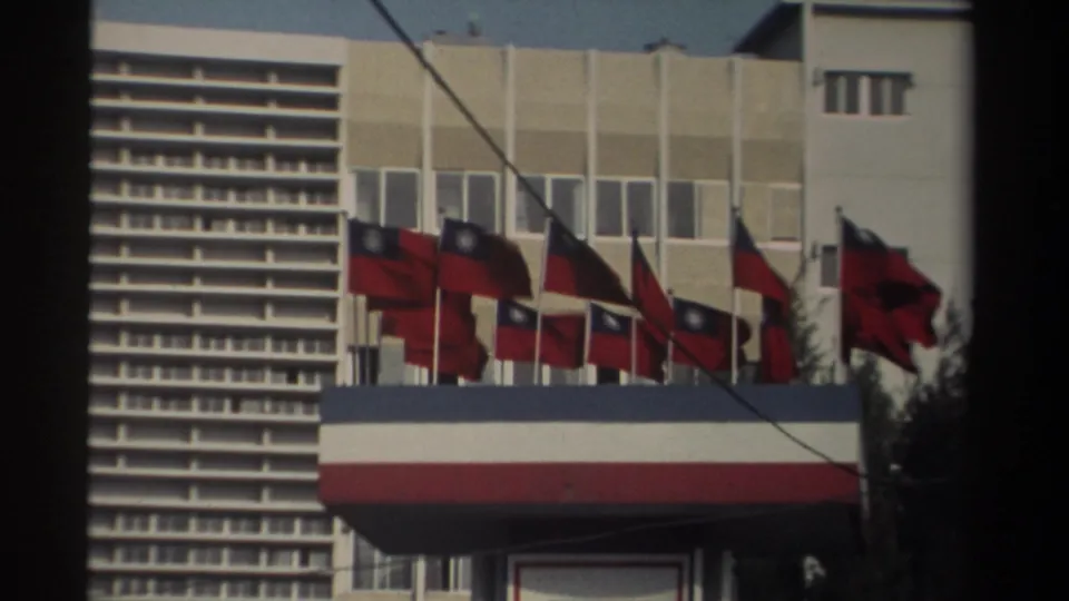 1982 Taiwan street view showing a modern building facade lined with multiple national flags and a striped awning in soft 8mm color.