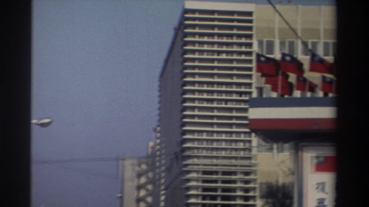 City street view with flags on a building edge and a tall high-rise beside the road.