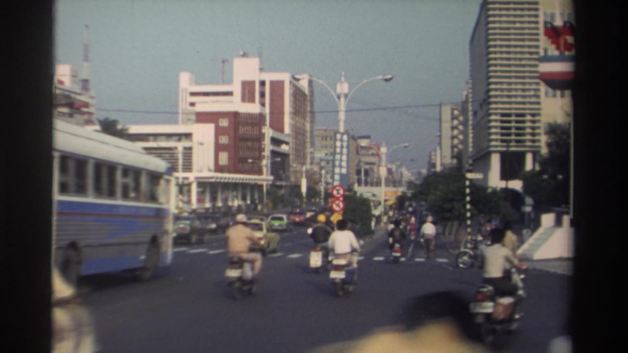 1982 Taiwan urban road view showing a blue-and-white public bus, scooters, cars, pedestrians, and dense mid-rise street architecture.