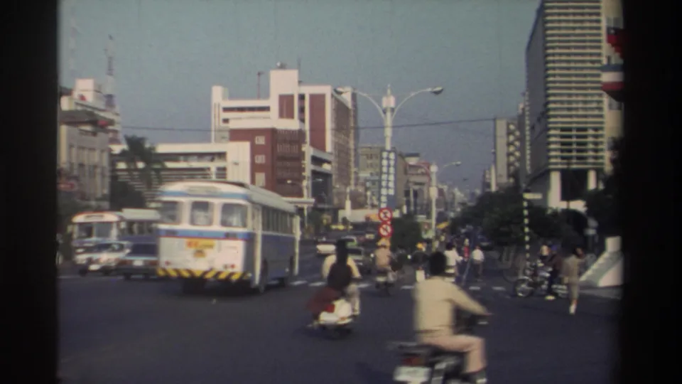 1982 Taiwan traffic scene with the rear of a blue-and-white bus, scooters, cars, pedestrians, street signs, and commercial buildings.