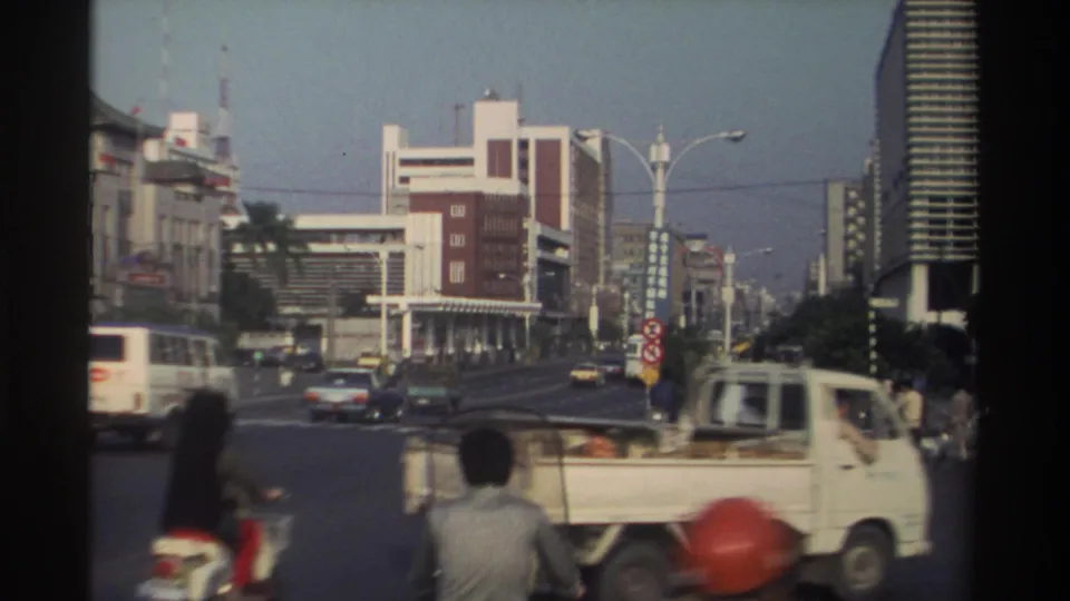 1982 Taiwan city intersection with a small truck in the foreground, a bus, cars, scooters, pedestrians, streetlights, and urban buildings.