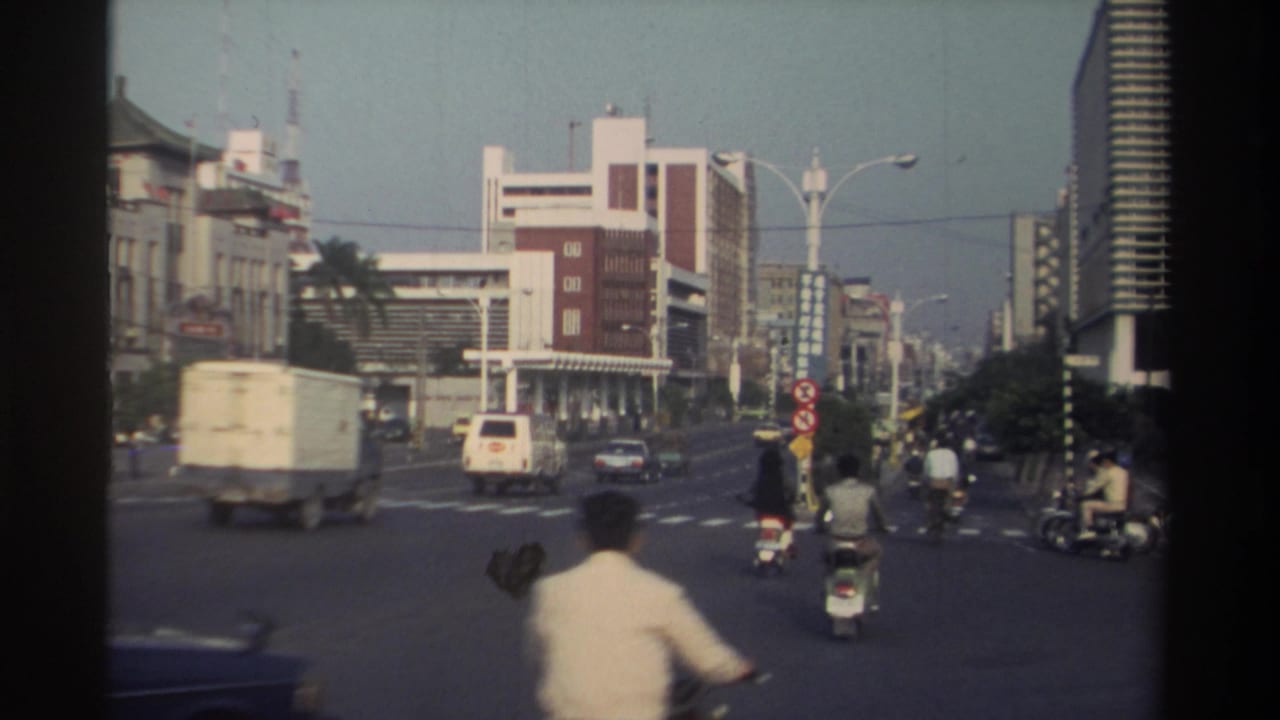 1982 Taiwan traffic scene with a box truck, van, scooters, and pedestrians moving across a large city intersection.