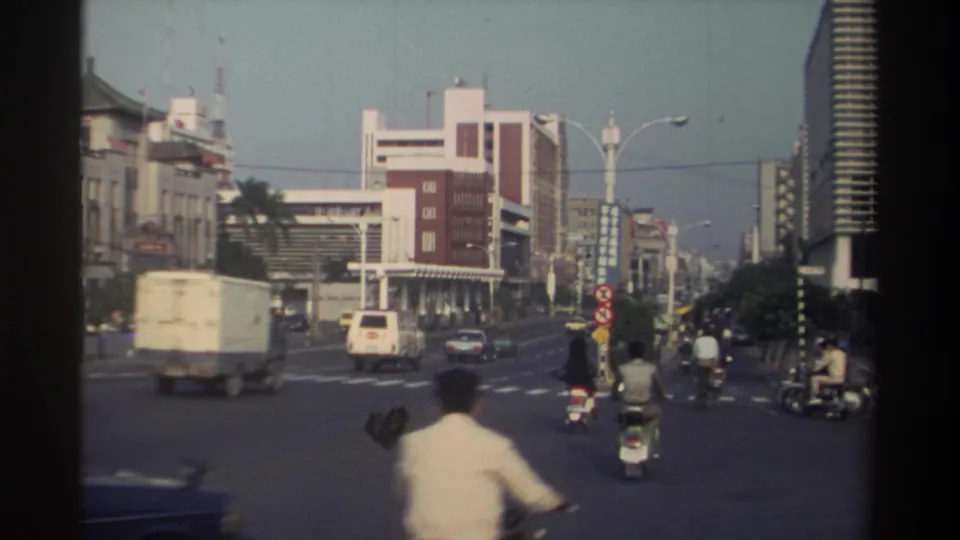1982 Taiwan traffic scene with a box truck, van, scooters, and pedestrians moving across a large city intersection.