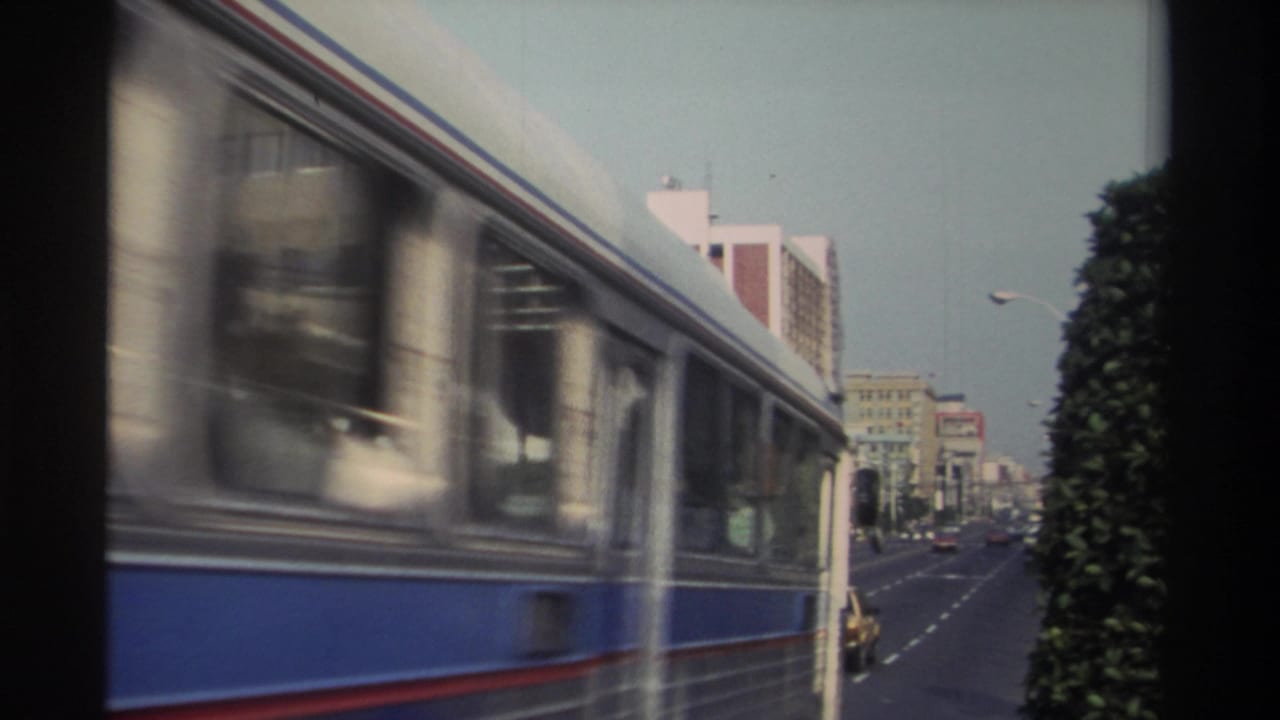 A blue-and-white bus moves past the camera on a Taiwan city street, partially obscuring traffic and buildings in the background.