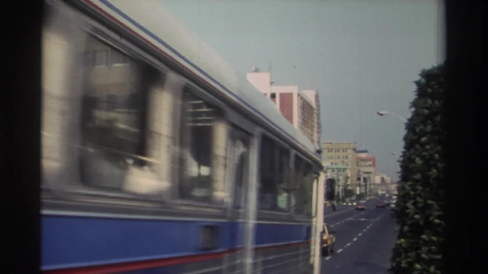 A blue-and-white bus moves past the camera on a Taiwan city street, partially obscuring traffic and buildings in the background.