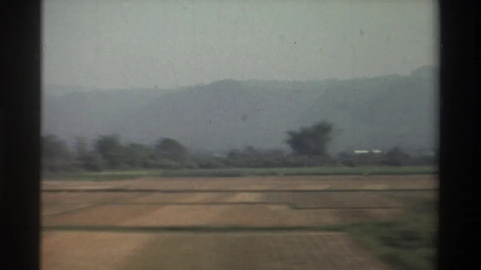 1982 Taiwan travel view from a moving vehicle, showing open fields, distant low hills, scattered trees, and a hazy horizon.