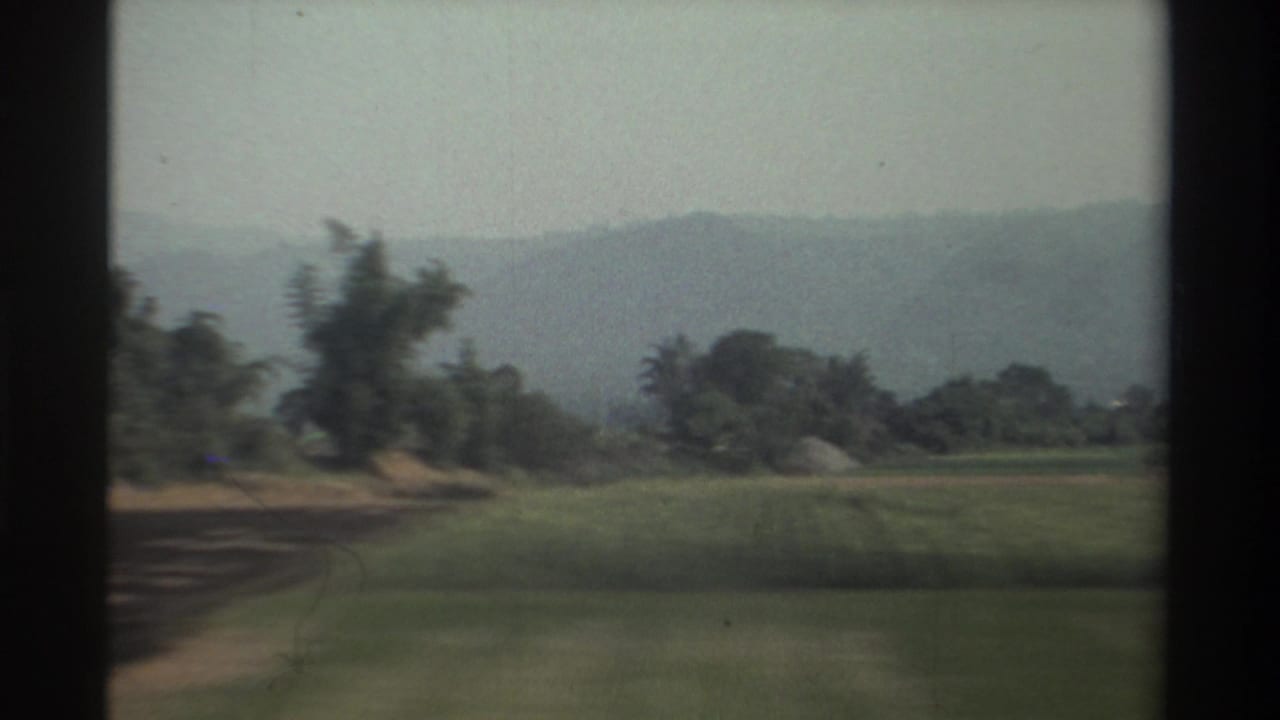 Green fields, roadside trees, and hazy hills framed by dark vertical window edges.