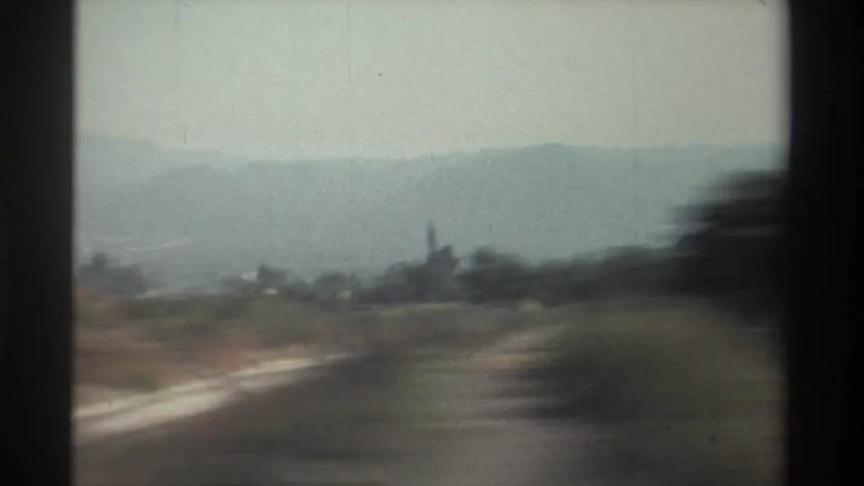 End frame of 1982 Taiwan countryside footage showing blurred roadside land, fields, trees, and hazy hills through a vehicle window.