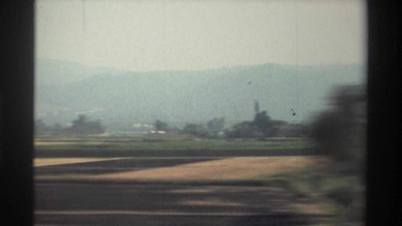 Farmland and distant hazy mountains seen past dark vertical window or film borders.