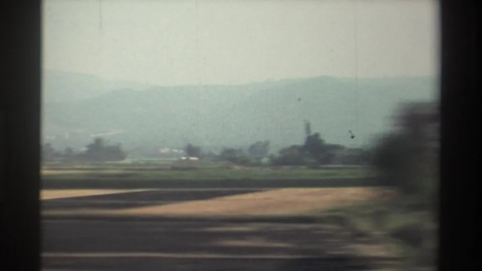 1982 Taiwan home-movie view of fields, hedges, distant misty hills, and a cloudy sky from a moving vehicle.