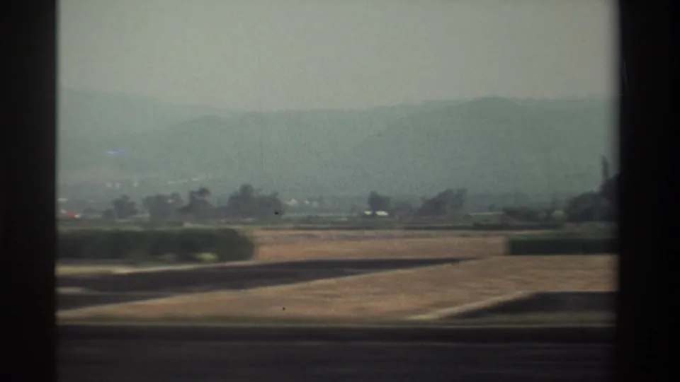 Rural Taiwan landscape from 1982 with cultivated fields, low vegetation, distant hills, and soft motion blur from travel.