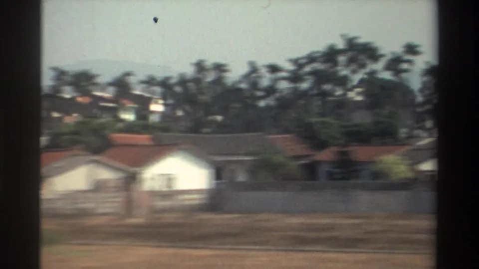 1982 Taiwan roadside scene with small white buildings, red roofs, palm trees, open foreground, and hazy hills in the background.