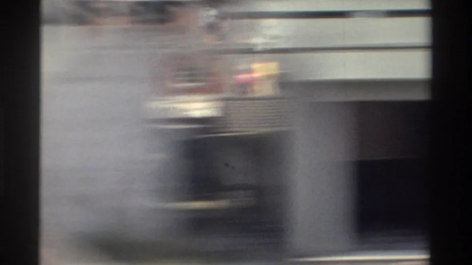 Blurred 1982 Taiwan home-movie frame with a pale roadside structure or passing vehicle edge, dark window framing, and strong motion smear.