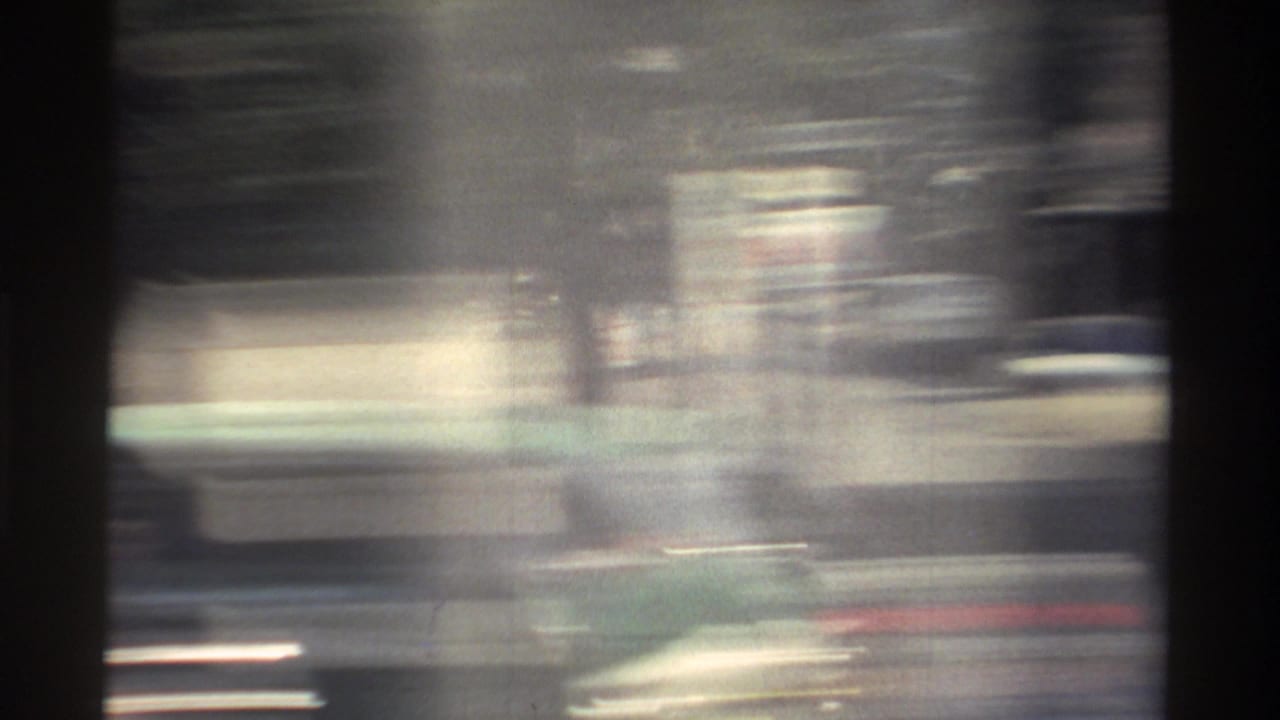 Blurred 1982 Taiwan roadside view from a moving vehicle, with streaked buildings, dark frame edges, and soft 8mm grain.