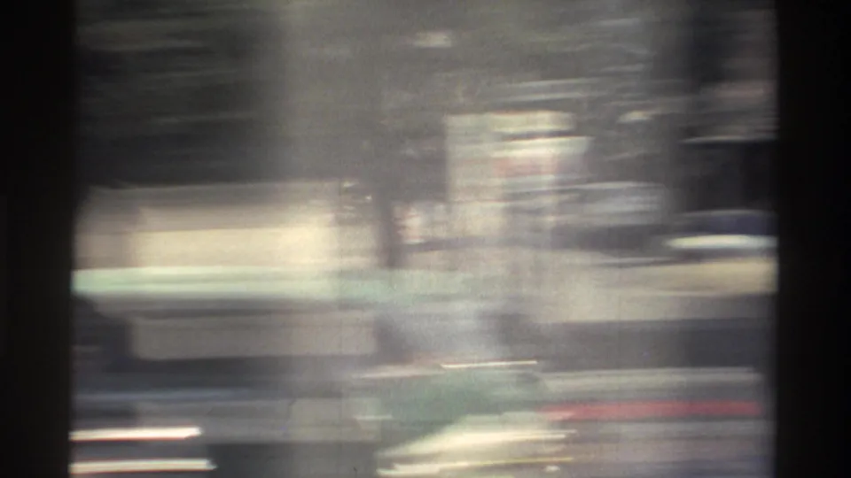 Blurred 1982 Taiwan roadside view from a moving vehicle, with streaked buildings, dark frame edges, and soft 8mm grain.