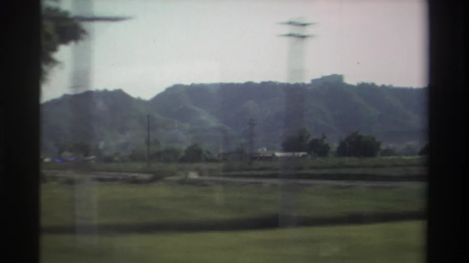 A moving 8mm view of Taiwan farmland in 1982 shows low wooded hills, fields, trees, and a utility tower softened by motion blur.