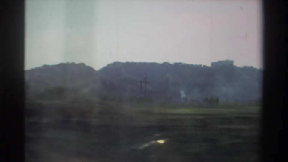 1982 Taiwan road-trip frame showing fields, utility poles, wooded hills, and distant structures from a moving vehicle.
