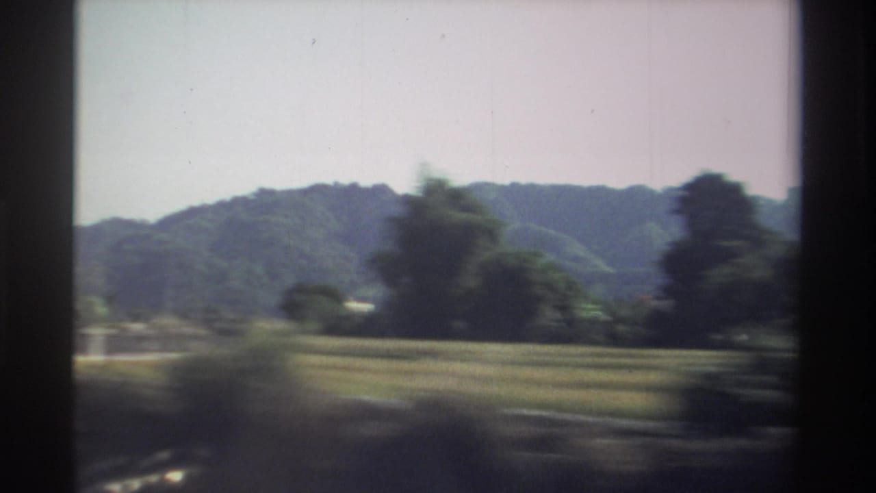 Forested hills, fields, and roadside trees blur past from a moving vehicle.