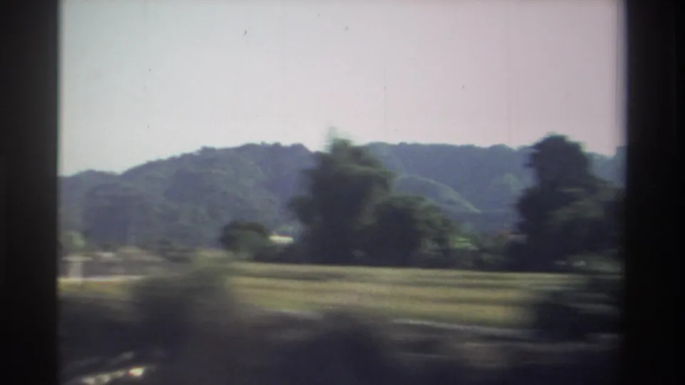 1982 Taiwan road-view frame with fields, roadside trees, and wooded hills softened by vehicle motion.