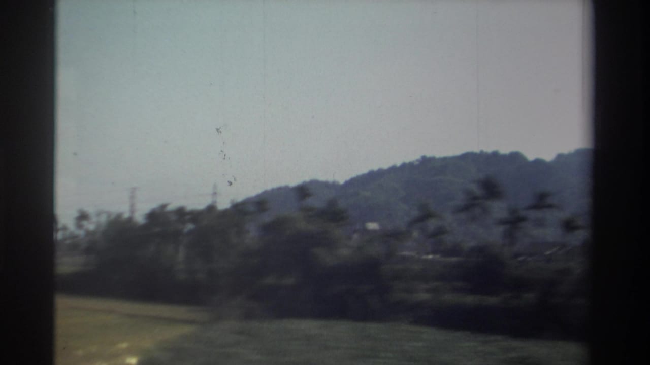 1982 Taiwan home-movie frame showing low mountains, fields, and roadside vegetation blurred by vehicle movement.