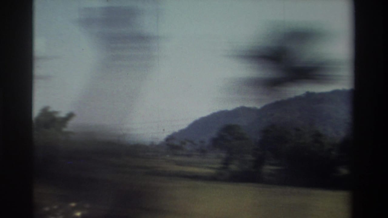 Distant hills and open fields pass behind blurred roadside trees.