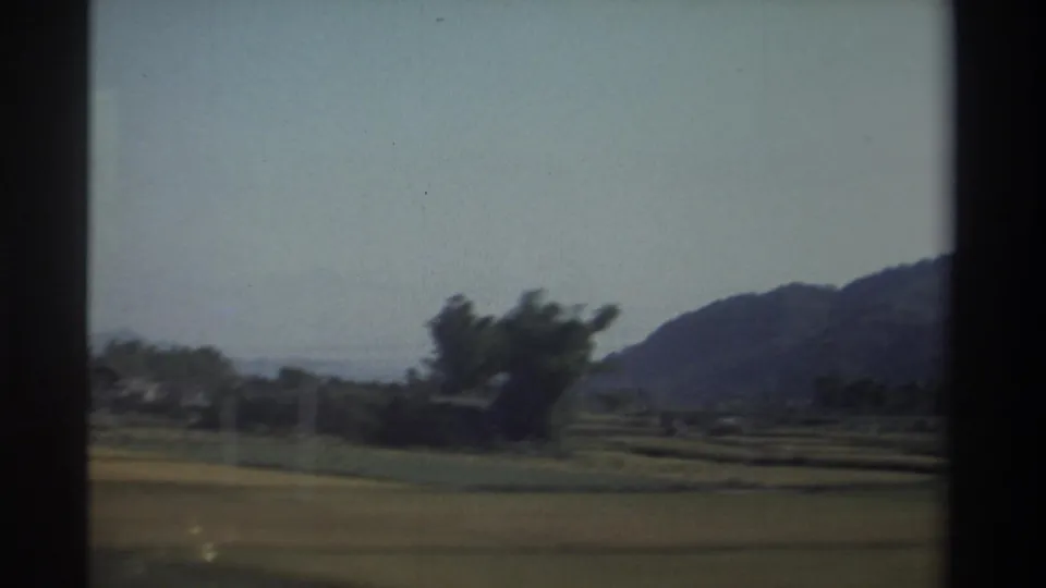 1982 Taiwan rural landscape frame with farmland, a rounded mountain slope, scattered trees, and softened vehicle motion.