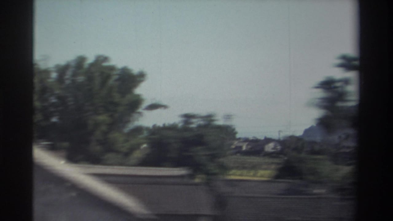 1982 Taiwan home-movie frame showing roadside trees, low rooftops, and a pale sky blurred by vehicle motion.