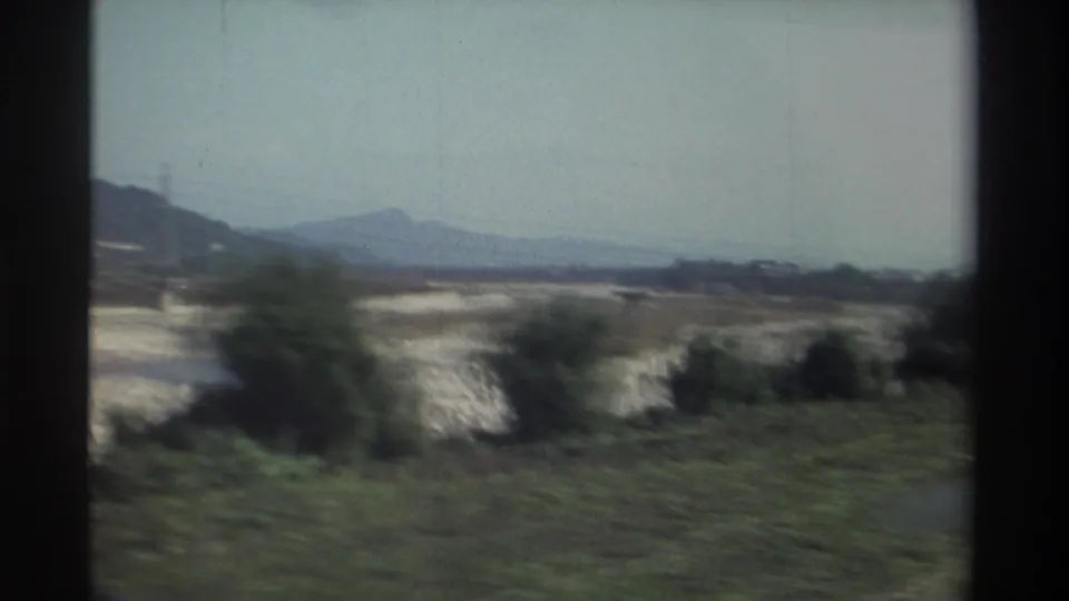 1982 Taiwan countryside frame with fields, shrubs, hazy mountains, and soft motion blur from a moving vehicle.