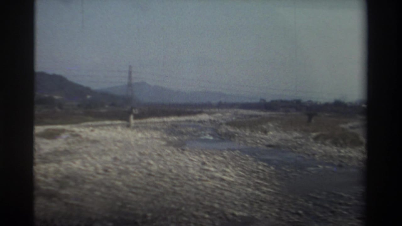 Dry rocky riverbed with a transmission tower and hills in the background.