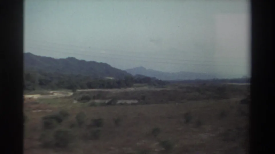 1982 Taiwan home-movie view of low hills, open vegetation, and a pale dry riverbed or road seen from a moving vehicle.