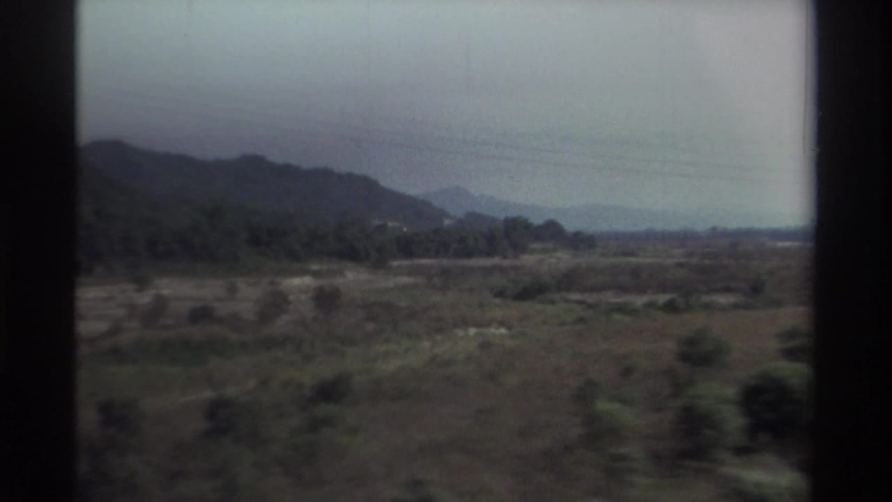 1982 Taiwan train-window view of hazy hills, open fields, and distant mountains with dark window borders.