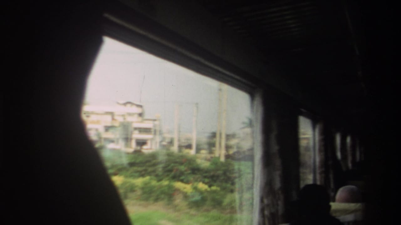 From inside a moving bus in Taiwan, the window shows low town buildings, greenery, and poles while passengers appear as dark silhouettes.