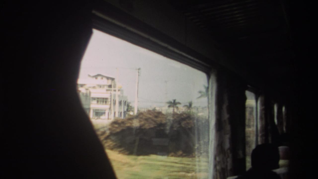 A Taiwan bus passenger view shows a pale roadside building, brush, utility poles, and the shadowed shape of another rider inside.