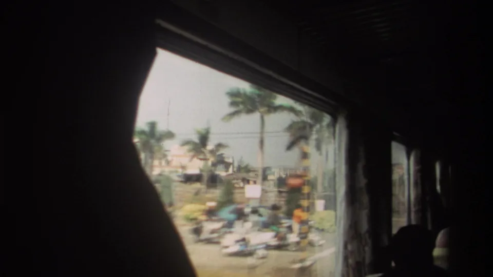 A moving bus window in Taiwan shows blurred street traffic, palm trees, signs, and roadside structures, with passengers in silhouette.