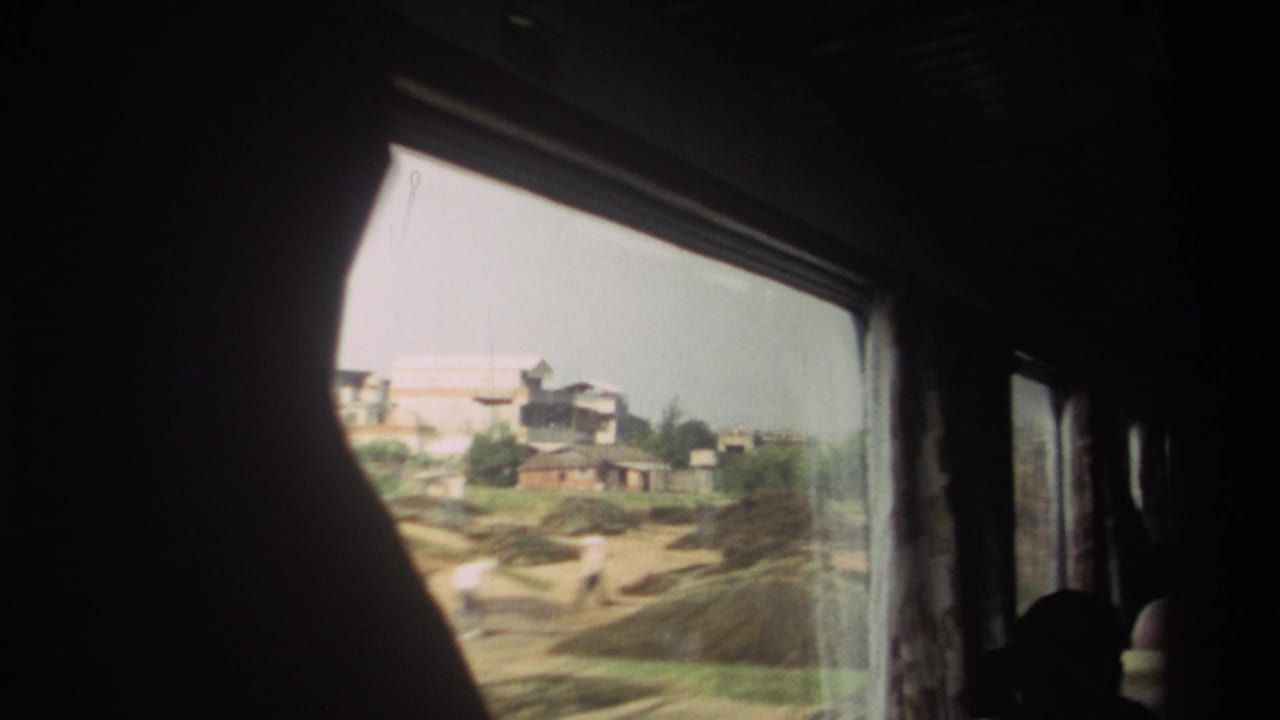 1982 Taiwan rail passenger view framed by a dark curtain, with low buildings and open trackside ground outside the window.