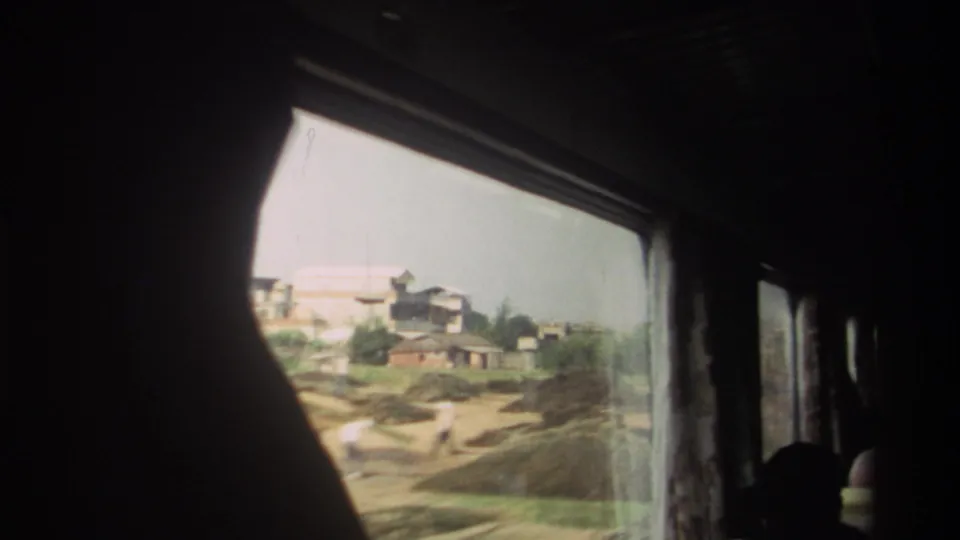 1982 Taiwan rail passenger view framed by a dark curtain, with low buildings and open trackside ground outside the window.