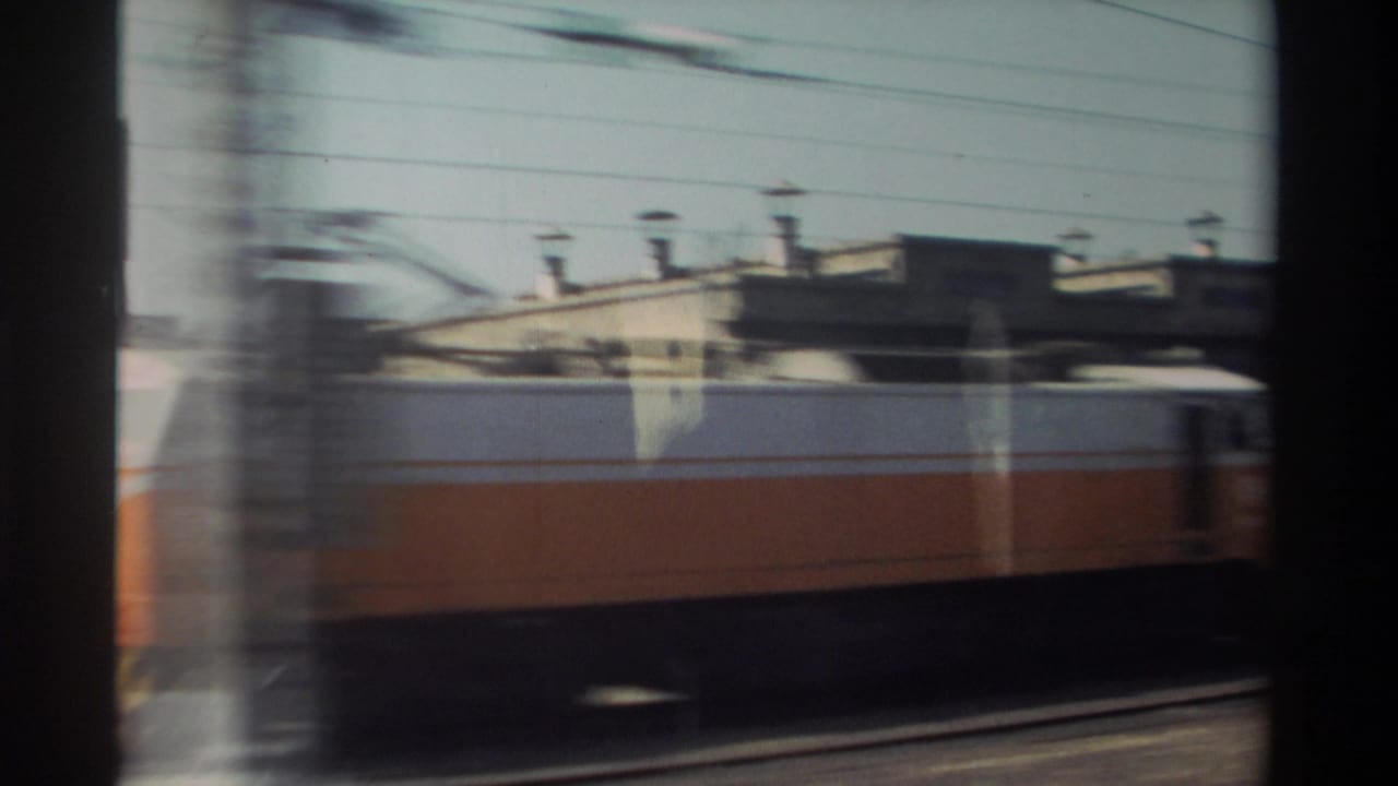 Yellow-and-white train passing on an adjacent track beside buildings.