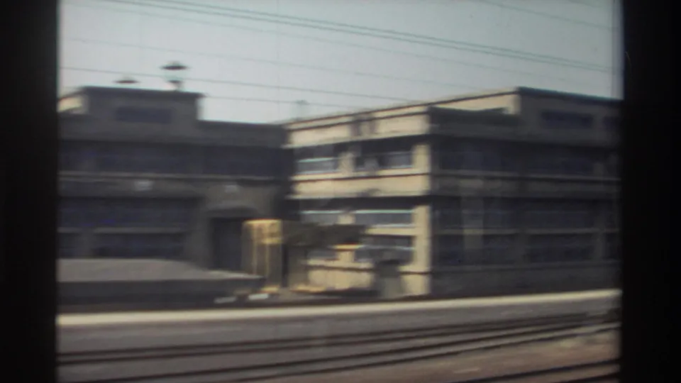 Train-window view of a low-rise rail-side building, tracks, and overhead wires in Taiwan, 1982.