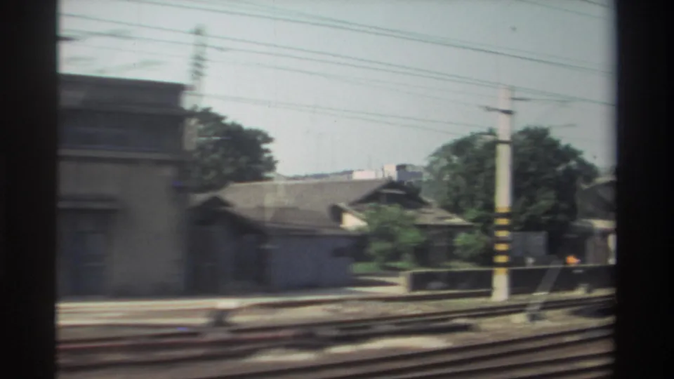1982 Taiwan rail-side view with small houses, trees, utility pole, and tracks passing by the train window.