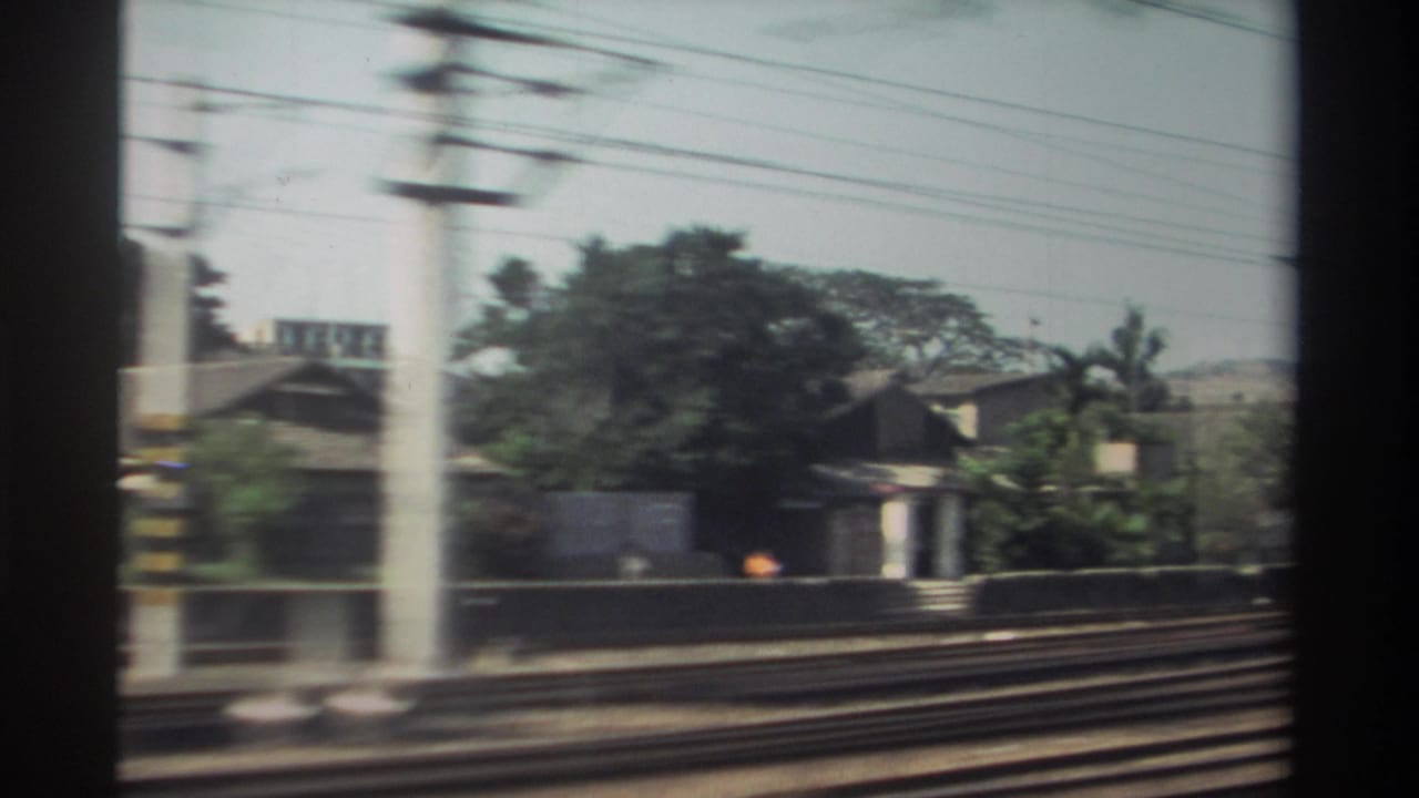 Train window view of tracks, utility poles, trees, and small buildings passing by.